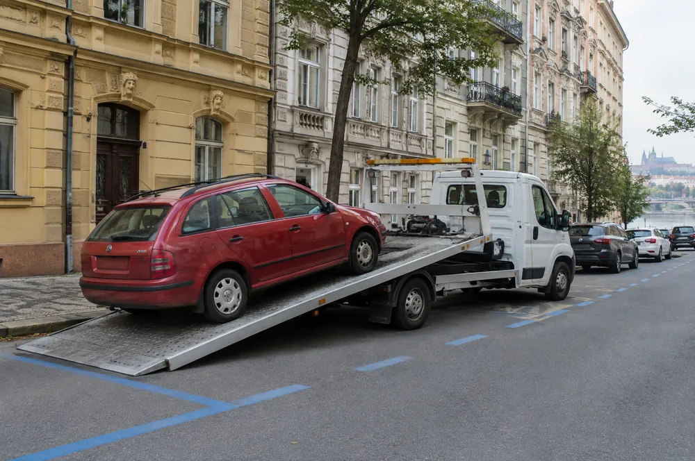 Bílá odtahovka nakládá červenou Škodu Fabii combi v ulici s modrou zónou na Smíchově